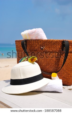 hat, bag, sun glasses and towel on a tropical beach with blue sky