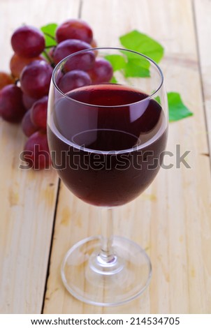 Glass filled with Red Grape Juice  and ripe sweet grape fruit on wooden plank table