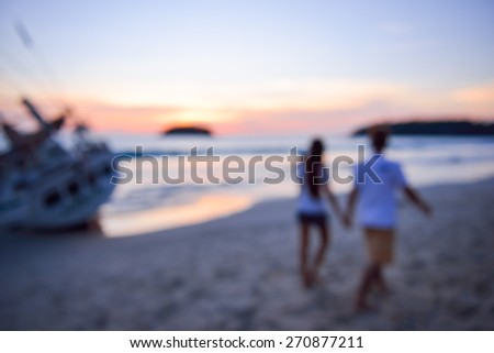 Blurred silhouette of couple walking hand in hand on sunset background, two people in love walking on the beach blur effect