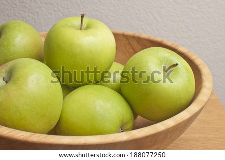 granny smith apples in wood bowl on wood table