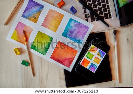 smartphone on arts hand drawn background with digital artist supplies: brushes, laptop, paper