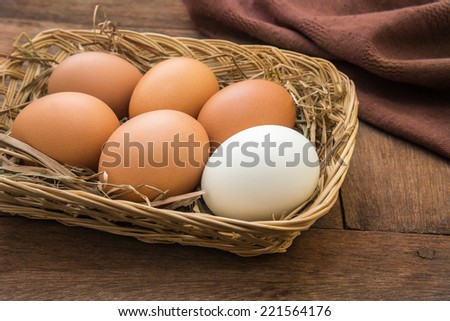White egg and brown eggs in basket