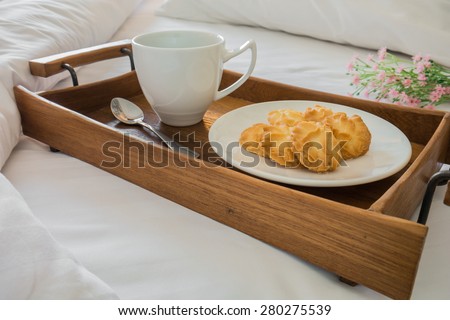 Butter cookies and coffee cup in wooden tray on comfortable bed