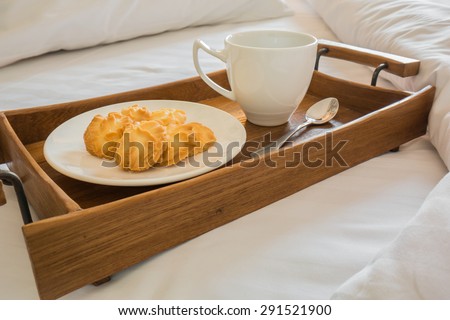 Butter cookies and coffee cup in wooden tray on comfortable bed