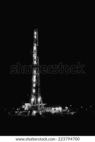 Drilling for oil 24 hrs a day, a rig runs all night with a full crew under the lights. Black and White image.
