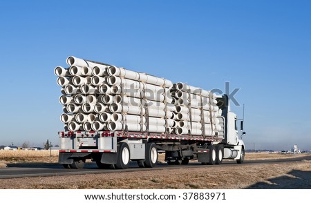Big truck with flatbed trailer hauling plastic pipe.