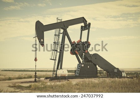 Pump jack starting the lifting stroke to brink crude oil up out of a producing oil well. Retro instagram look.