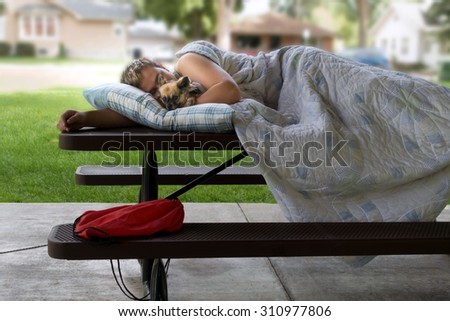 Homeless man sleeping on a picnic table in the city park holding his pet dog.