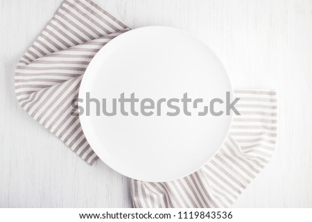 Empty white circle plate on wooden table with linen napkin. Overhead view.