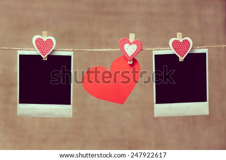 Two polaroid photo frames and heart for valentines day hanging on vintage background with vintage instagram toning