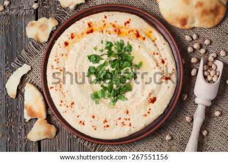 Appetizer creamy hummus tasty traditional food with tahini paste, olive oil, paprika and parsley in rustic plate on vintage wooden background
