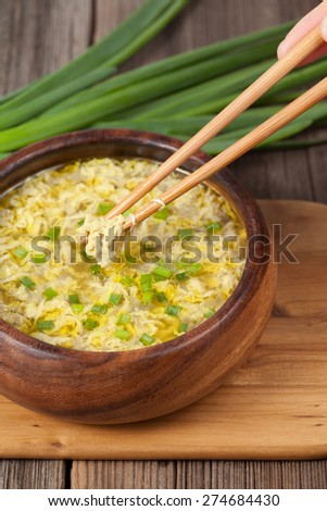 Unrecognizable man holding in hand chopsticks with asian egg flour soup in wooden dish