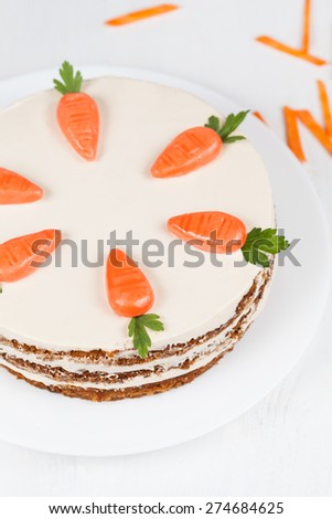 Plate with carrot sponge cake with little orange carrots and cream on white background