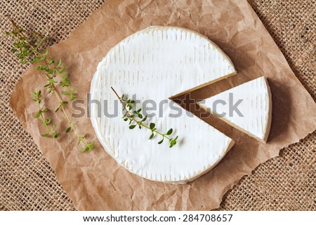 Sliced round camembert cheese traditional milk creamy dairy product with thyme on vintage parchment. Rustic style and natural light. Top view. Rustic sacking textile background.