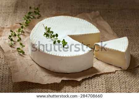 Sliced camembert cheese, creamy round traditional organic healthy French dairy gourmet food with thyme on rustic parchment and vintage sacking cloth table background. Rustic style and natural light.