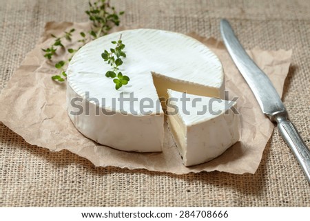 Camembert cheese, sliced round creamy traditional Normand French dairy milk food with vintage knife and thyme on rustic parchment. Natural light, rustic style.