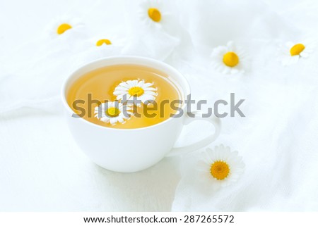 White cup of natural healthy chamomile herb tea with fresh camomile flowers on rustic kitchen table background. Rustic style and natural liught