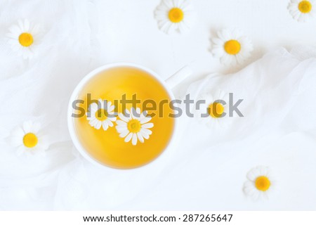Healthy natural chamomile herbal yellow tea in a white cup with blooming camomile flowers on white kitchen table background. Natural light and rustic style.