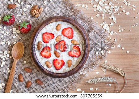 Healthy prepared oatmeal porridge breakfast with strawberries and nuts in wooden bowl on vintage table background. Rustic style and natural light.