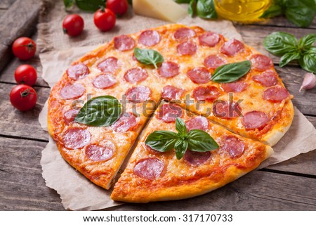 Sliced homemade Italian traditional pepperoni pizza with basil, salami, mozzarella cheese and tomato sauce on vintage wooden table background. Rustic style and natural light.