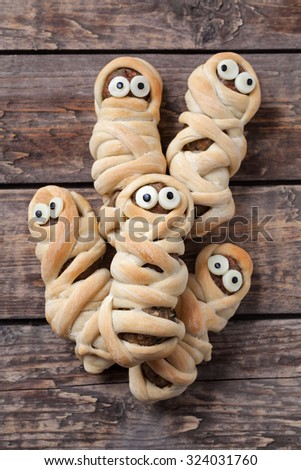 Scary halloween mummy sausages wrapped in dough with funny eyes for celebration party decoration. Vintage wooden background. Rustic style.