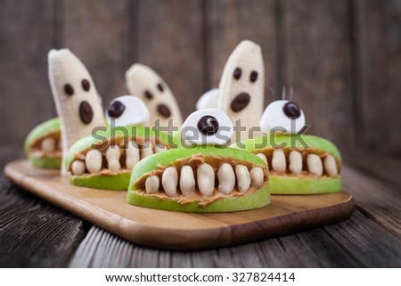 Scary edible halloween treat apple cyclop mouth with peanut butter teeth and banana ghosts chocolate face. Healthy natural vegetarian dessert recipe. Homemade party decoration sweets