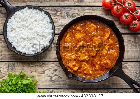 Chicken tikka masala traditional Asian spicy meat food with rice tomatoes and parsley in cast iron pan on vintage wooden background