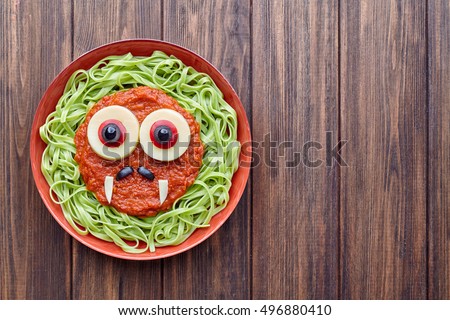 Green spaghetti pasta scary halloween food vampire monster with smile, fake blood tomato sauce moustaches and funny big mozzarella eyeballs decoration kid party meal on vintage table