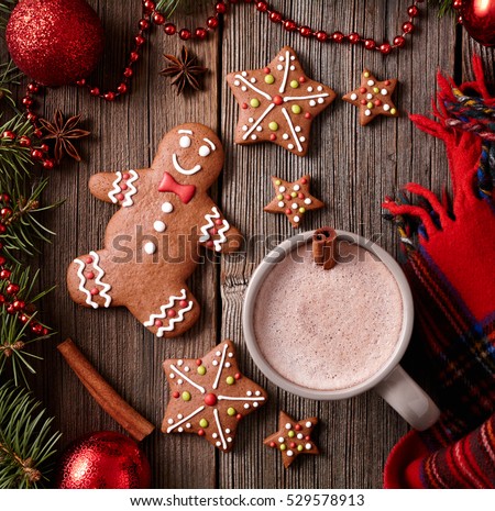 Cup of hot chocolate or cocoa with gingerbread man, warm scarf composition in fir tree decorations frame on vintage wooden table background. Square view