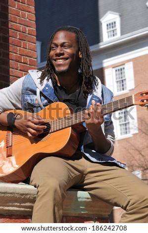happy young black man playing the guitar in the city