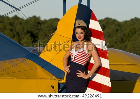 beautiful young pinup girl posing next to a vintage biplane aircraft