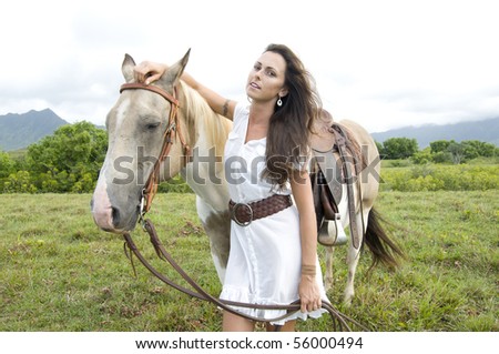 beautiful young woman holding a horse by the rains in a Kauai ranch