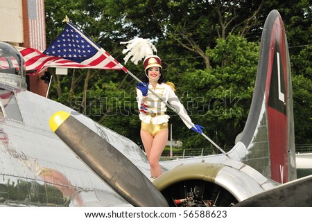 beautiful marching band majorette standing on the wings of a bomber and holding the American flag