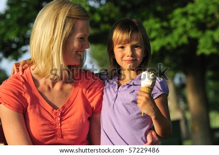 happy mom and daughter sharing an ice cream in the park