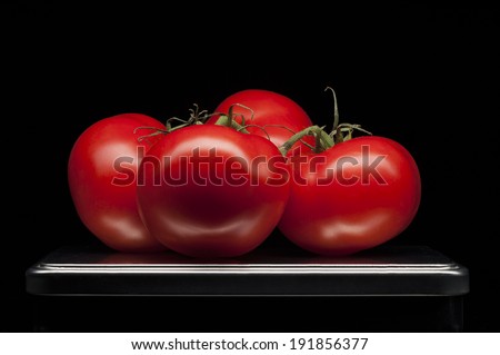 On tray four red ripe tomatoes with luxury black background. Clean line