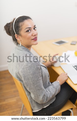 Happy young woman sitting on a wood chair behind a wood desk with cup of coffee in her hand. Copy space