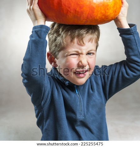 Closeup of little boy making a face with heavy orange pumpkin hat. Halloween theme. Studio shoot after freshly harvest in autumn. Color image