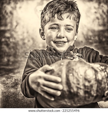 Head and shoulders portrait of little boy holding a big ripe pumpkin. Halloween theme. Studio shoot after freshly harvest in autumn. Sepia toned