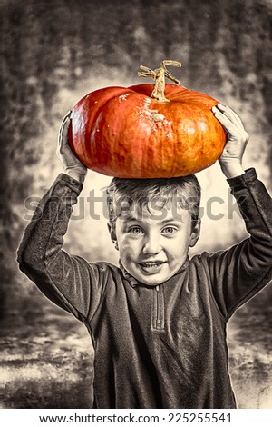 Portrait of little boy holding with difficulty an orange heavy pumpkin on his head. Halloween theme. Studio shoot after freshly harvest in autumn. Mixed sepia and color image