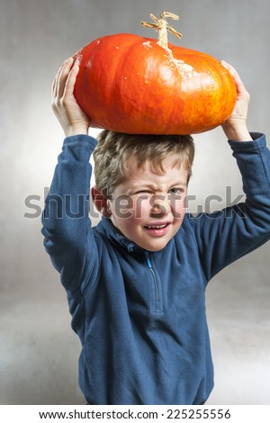 Portrait of little boy making a face with heavy orange pumpkin hat. Halloween theme. Studio shoot after freshly harvest in autumn. Color image