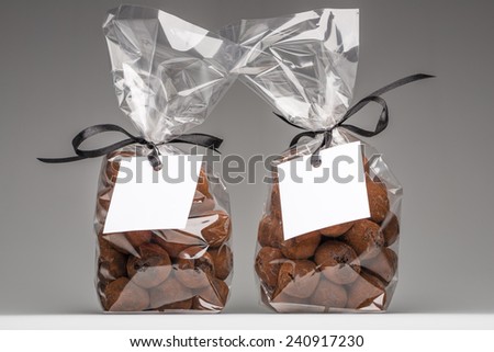 Two luxury plastic bags with elegant black ribbons of chocolate truffles. Blank label that you can add your own trademark or your own message. Christmas gifts. Shooting on grey background in studio.