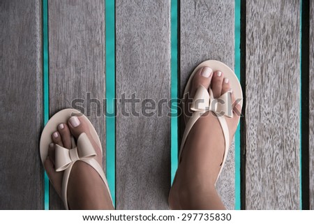Groomed female feet with a pedicure in beige beach shoes on wooden bridge with turquoise water of pacific ocean underneath. View from above. Summer concept holiday,Vintage style
