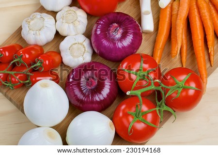 Red onion, carrots, white onion, tomatos, carrot and garlic on a wooden board