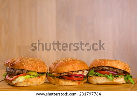 Tasty burger with melted cheese and a thick succulent ground beef patty garnished with lettuce, tomato, onion and rocket on a sesame bun standing on a picnic table in the garden