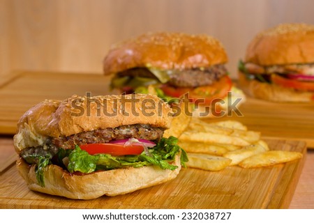 Tasty burger with melted cheese and a thick succulent ground beef patty garnished with lettuce, tomato, onion and rocket on a sesame bun standing on a picnic table in the garden