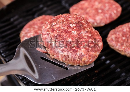 Preparing a batch of ground beef patties on grill or BBQ with one of them on spatula