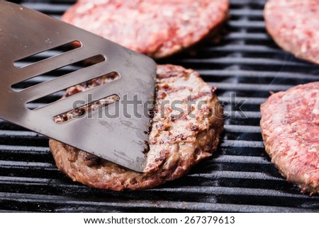 Preparing a batch of ground beef patties on grill or BBQ with one of them on spatula