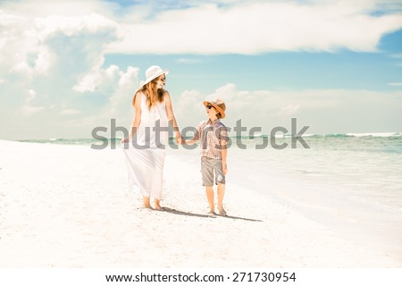 Happy beautiful mother and son walking along the beach in a sunny day