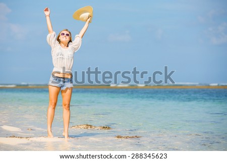 Young skinny caucasian girl at the beach waving with white hat over blue sky and pure ocean water on background. Travel, vacation, holidays, paradise concept, copyspace