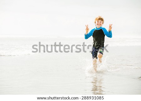 Young boy in swimming shorts and rash vest runs along Bali beach near sunset with reflection in the water